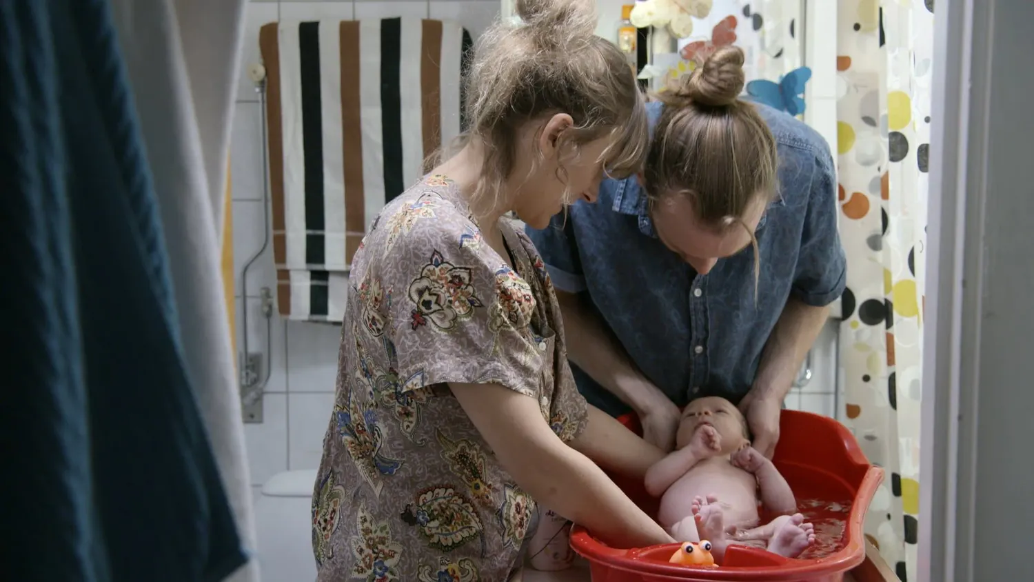 Parents bathing their baby in a red tub, Libero YouTube tutorial